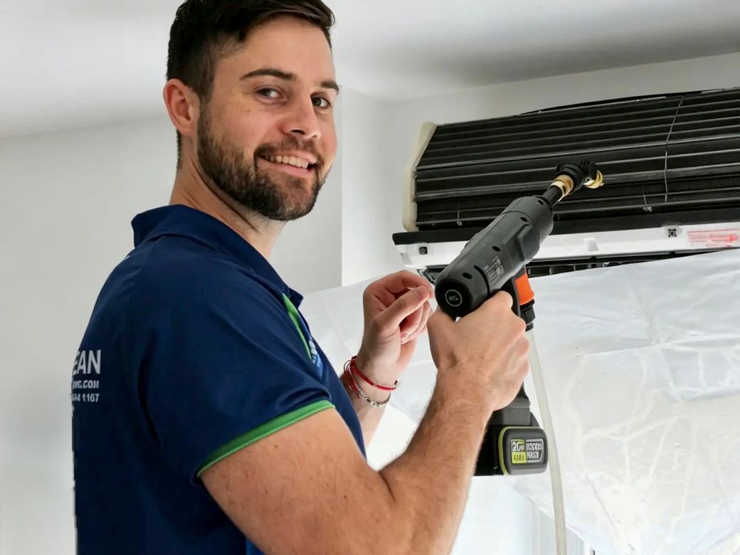 Green Clean technician spray-cleaning an air conditioning unit behind protective sheeting