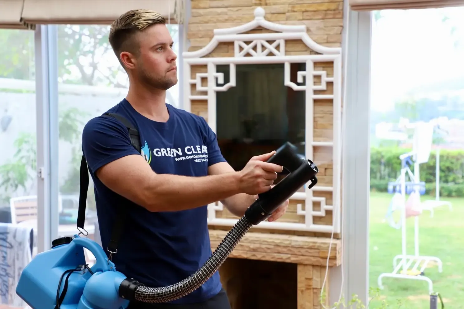 Green Clean technician holding a disinfection fogging machine beside a decorative window