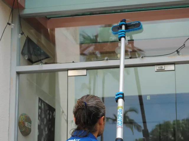 Green Clean cleaner using a pole squeegee to clean a glass door from outside