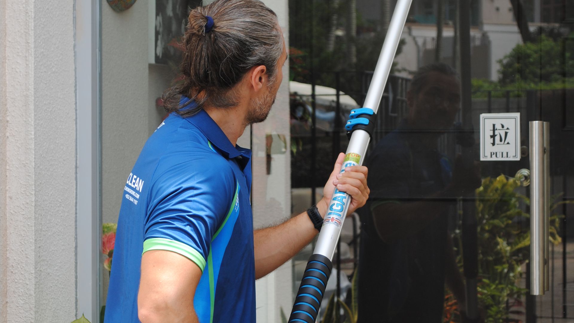 Green Clean cleaner holding a window-cleaning pole beside a Hong Kong terrace window